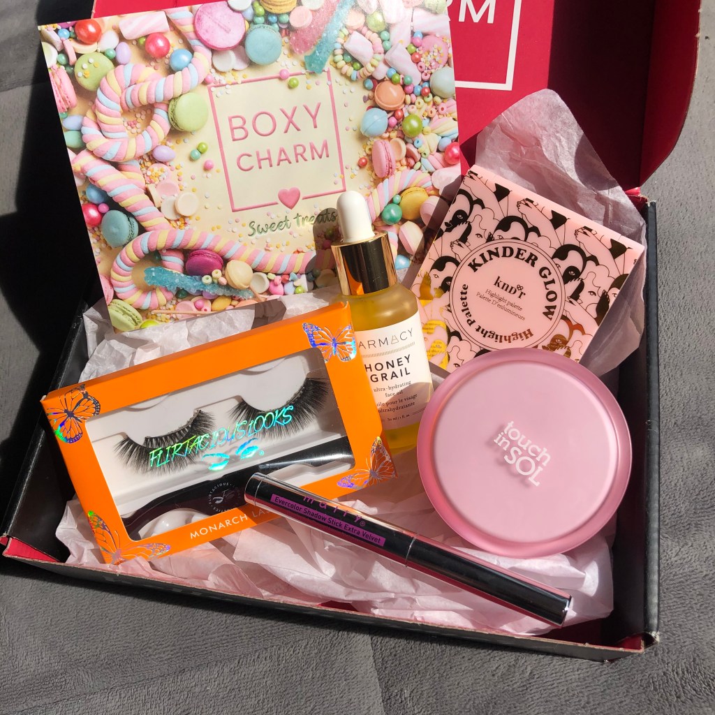 On of the variations of Boxycharm's April box, a beauty subscription service. Products include a pair of Flirtacious lashes, Mally Beauty eyeshadow stick, Touch in Sol face primer, Farmacy face oil and KNDR highlight palette. 